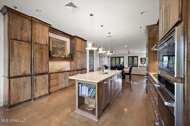 kitchen featuring concrete floors, appliances with stainless steel finishes, sink, hanging light fixtures, and a kitchen island with sink