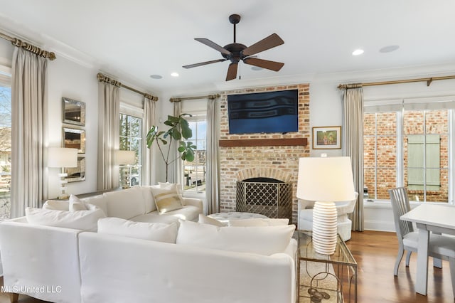 living room featuring ceiling fan, wood-type flooring, ornamental molding, and a brick fireplace