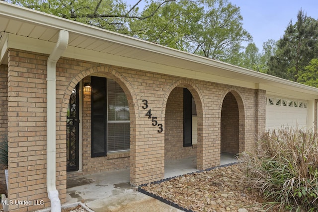 view of exterior entry with brick siding, an attached garage, and covered porch