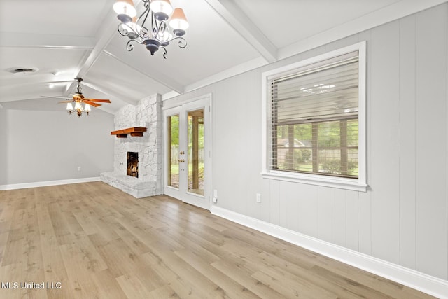 unfurnished living room with light wood-style floors, ceiling fan with notable chandelier, lofted ceiling with beams, a stone fireplace, and baseboards