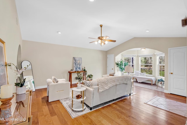 living room with lofted ceiling, light wood finished floors, baseboards, and arched walkways