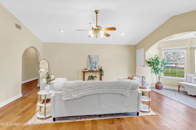 living area featuring vaulted ceiling, light wood-type flooring, arched walkways, and visible vents