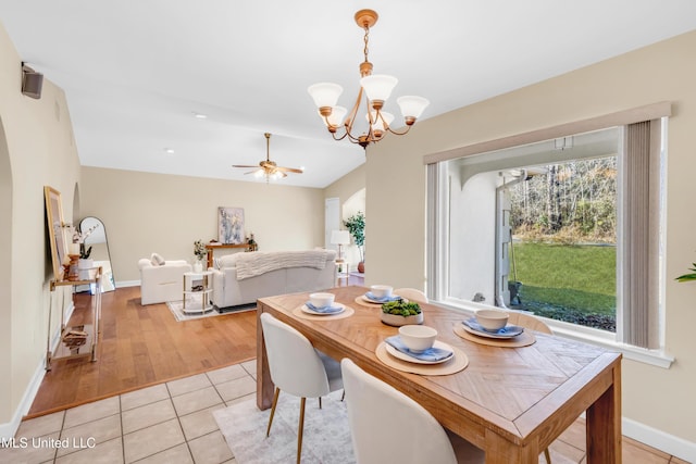 dining space with arched walkways, light tile patterned flooring, vaulted ceiling, baseboards, and ceiling fan with notable chandelier