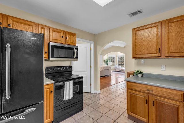 kitchen featuring light tile patterned floors, visible vents, arched walkways, light countertops, and black appliances