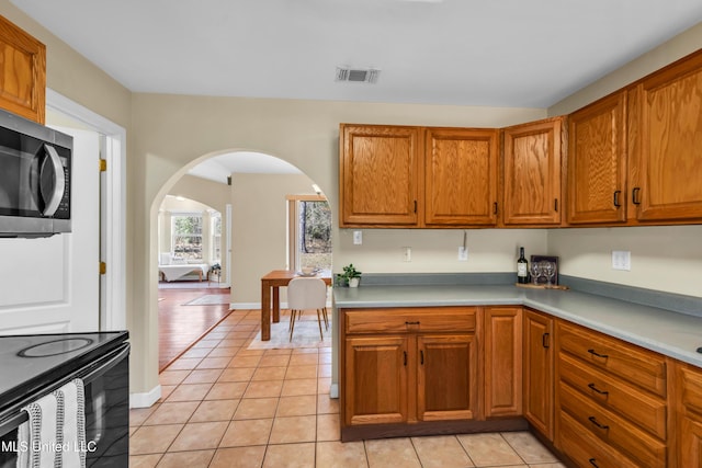 kitchen featuring arched walkways, light tile patterned flooring, stainless steel microwave, visible vents, and brown cabinetry