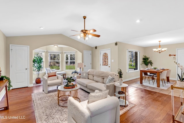 living room featuring arched walkways, lofted ceiling, ceiling fan with notable chandelier, baseboards, and light wood finished floors