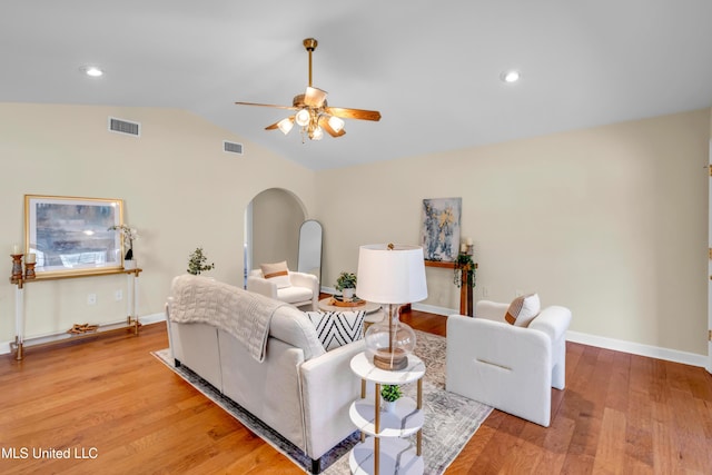 living area with arched walkways, light wood finished floors, vaulted ceiling, and visible vents