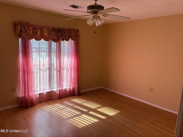 spare room featuring wood finished floors, visible vents, ceiling fan, and baseboards