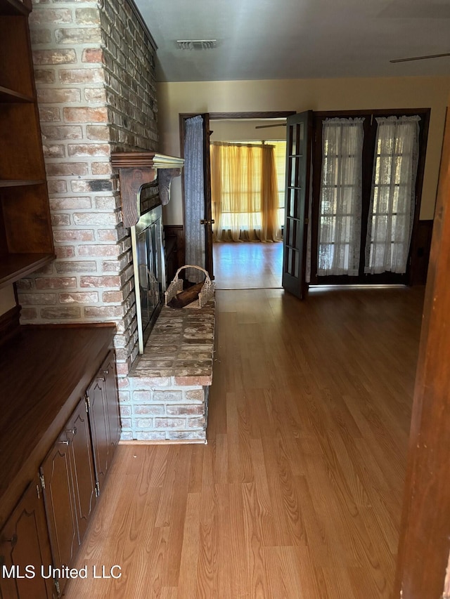 unfurnished living room featuring visible vents, wood finished floors, and a brick fireplace
