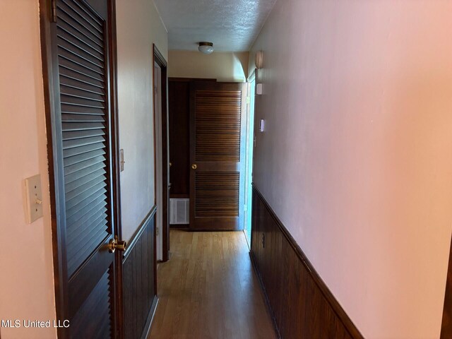 hallway with visible vents, wainscoting, wood finished floors, and a textured ceiling