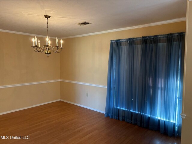 empty room featuring visible vents, a chandelier, wood finished floors, and baseboards