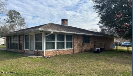 rear view of house with a chimney, a sunroom, and a lawn