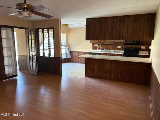 kitchen featuring black range with electric stovetop, light wood-type flooring, a wainscoted wall, a peninsula, and light countertops