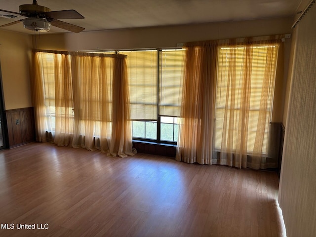 empty room with visible vents, wood finished floors, a ceiling fan, and wainscoting