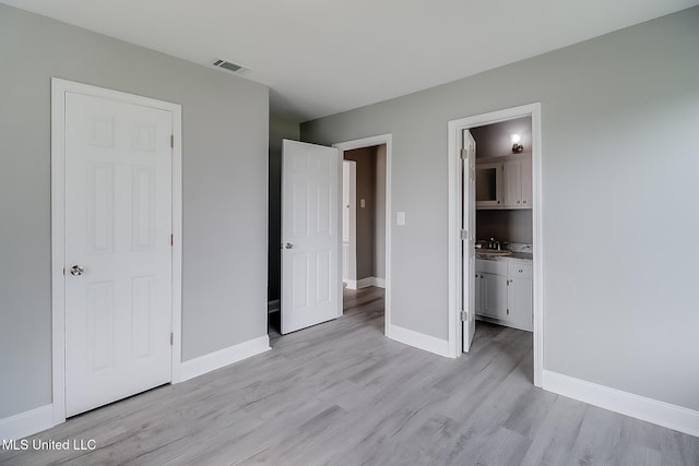 unfurnished bedroom with light wood-type flooring and connected bathroom