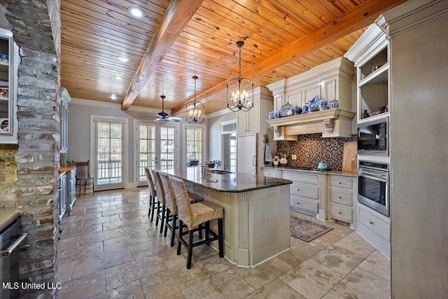 kitchen featuring decorative backsplash, stainless steel oven, cream cabinets, a center island with sink, and pendant lighting