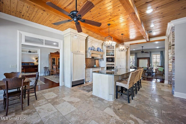 kitchen featuring oven, beam ceiling, an island with sink, pendant lighting, and tasteful backsplash