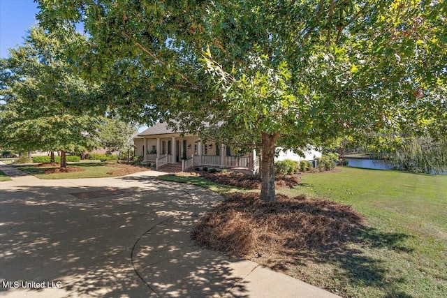 view of property hidden behind natural elements featuring a front yard, covered porch, and a water view