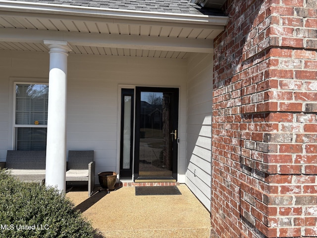 property entrance featuring a shingled roof and brick siding