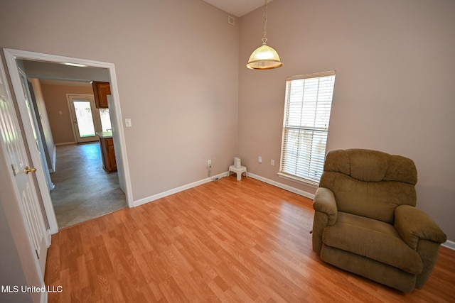 sitting room featuring light wood finished floors, baseboards, and high vaulted ceiling
