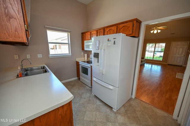 kitchen with a sink, white appliances, brown cabinets, light countertops, and baseboards