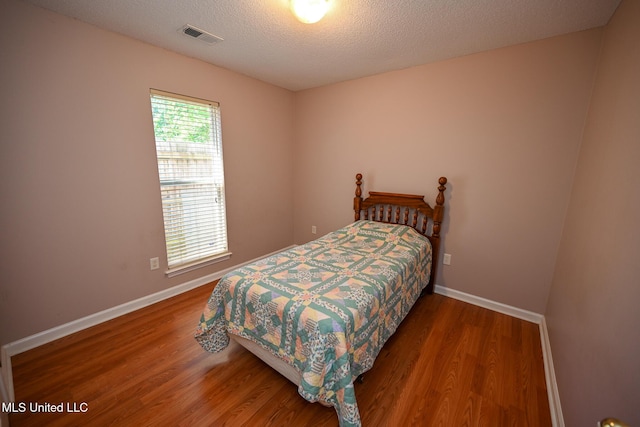 bedroom with baseboards, visible vents, and wood finished floors