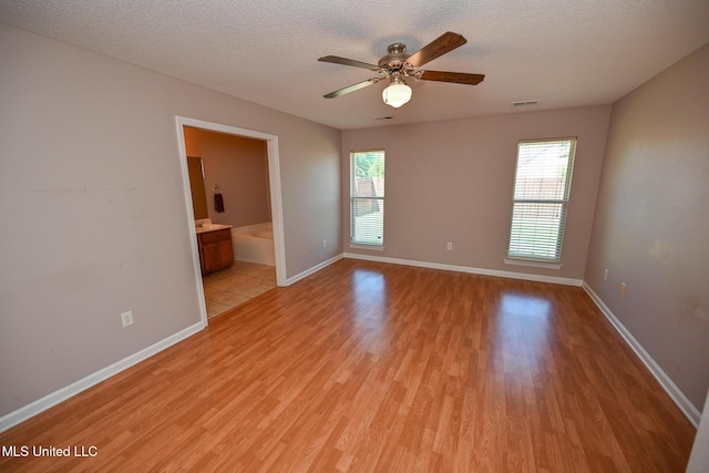 unfurnished room featuring a textured ceiling, light wood-type flooring, a healthy amount of sunlight, and visible vents