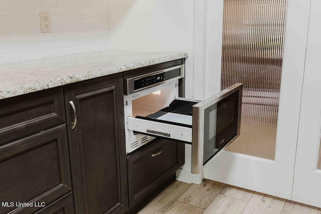 details with decorative backsplash, light stone countertops, light wood finished floors, and dark brown cabinets