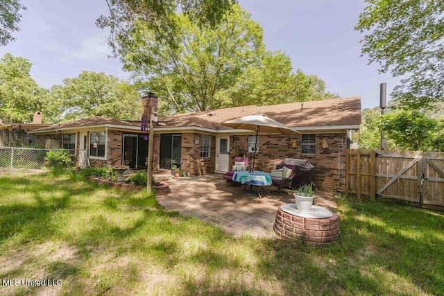 back of house featuring a chimney, brick siding, a fenced backyard, a yard, and a patio