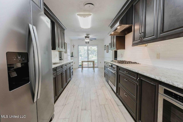 kitchen featuring ceiling fan, backsplash, light stone countertops, light wood finished floors, and stainless steel appliances