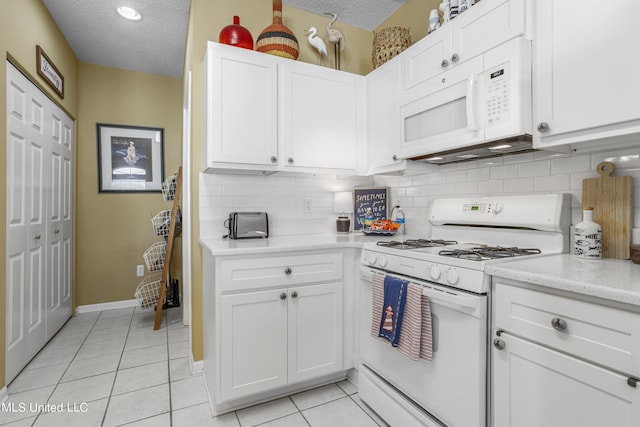 kitchen featuring a textured ceiling, light tile patterned floors, white cabinets, and white appliances