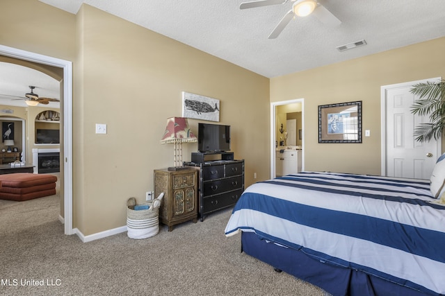 bedroom featuring carpet, ensuite bath, ceiling fan, a fireplace, and a textured ceiling