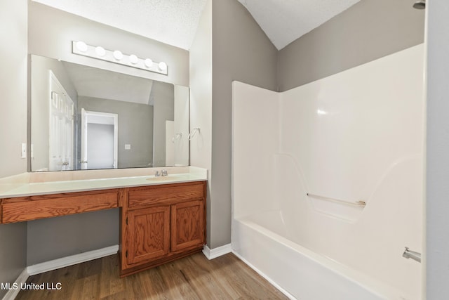 bathroom featuring vanity, wood finished floors, baseboards, bathtub / shower combination, and a textured ceiling