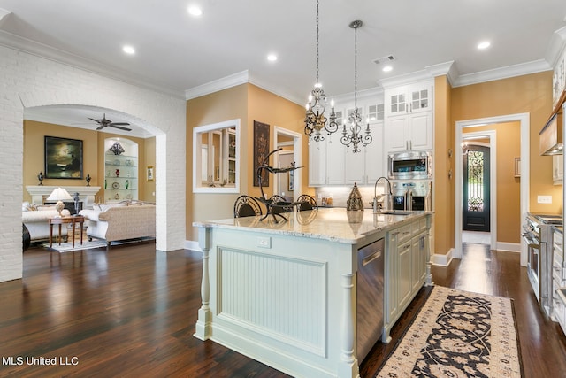 kitchen featuring dark wood-type flooring, a center island with sink, pendant lighting, appliances with stainless steel finishes, and light stone counters