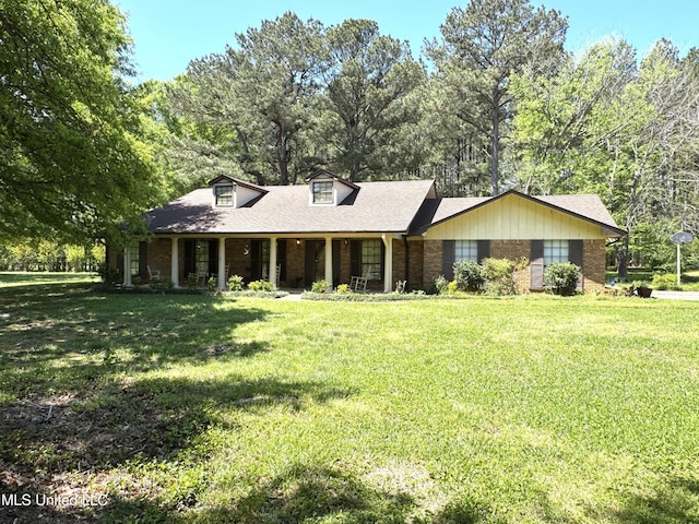 view of front facade with roof with shingles, covered porch, a front yard, and brick siding