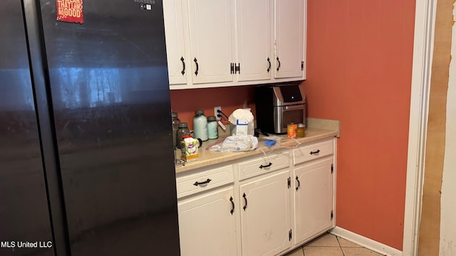 kitchen with white cabinetry, black refrigerator, and light tile patterned floors