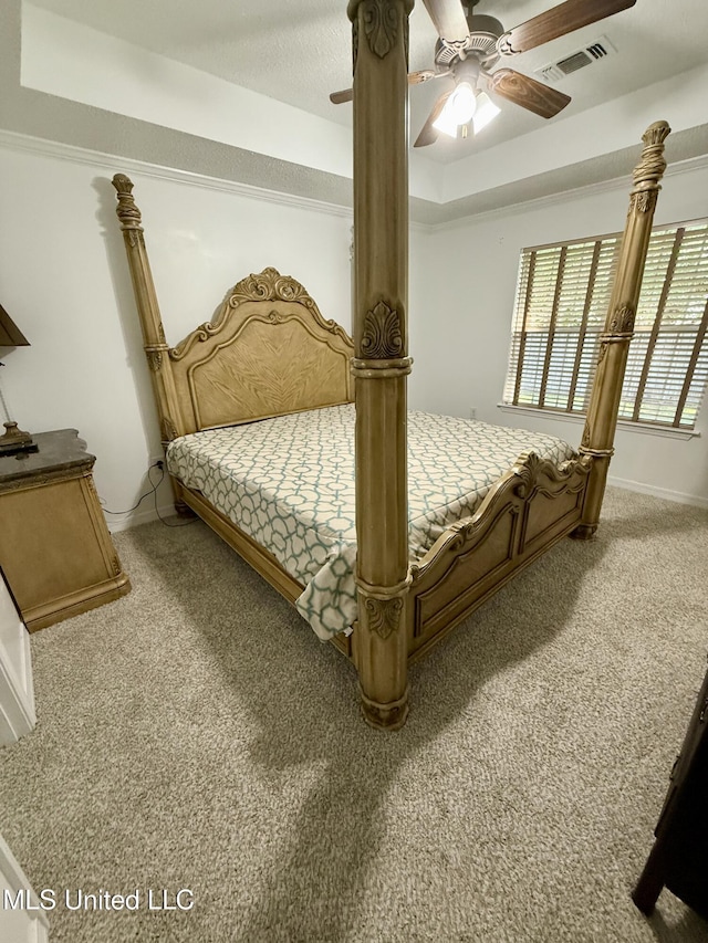 bedroom featuring a ceiling fan, visible vents, carpet floors, baseboards, and a tray ceiling