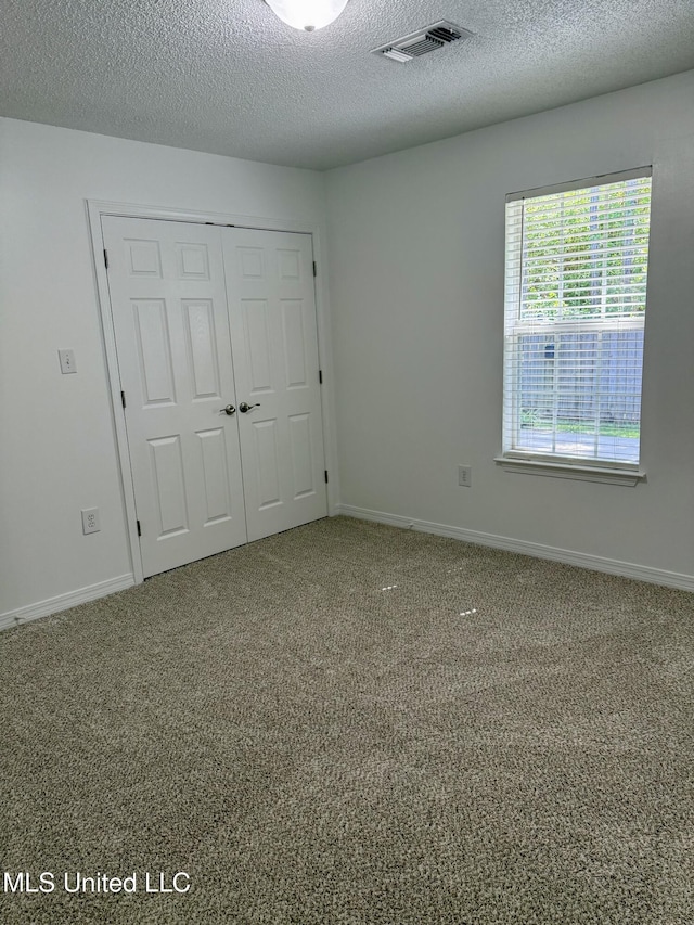 unfurnished room featuring baseboards, carpet, a textured ceiling, and visible vents
