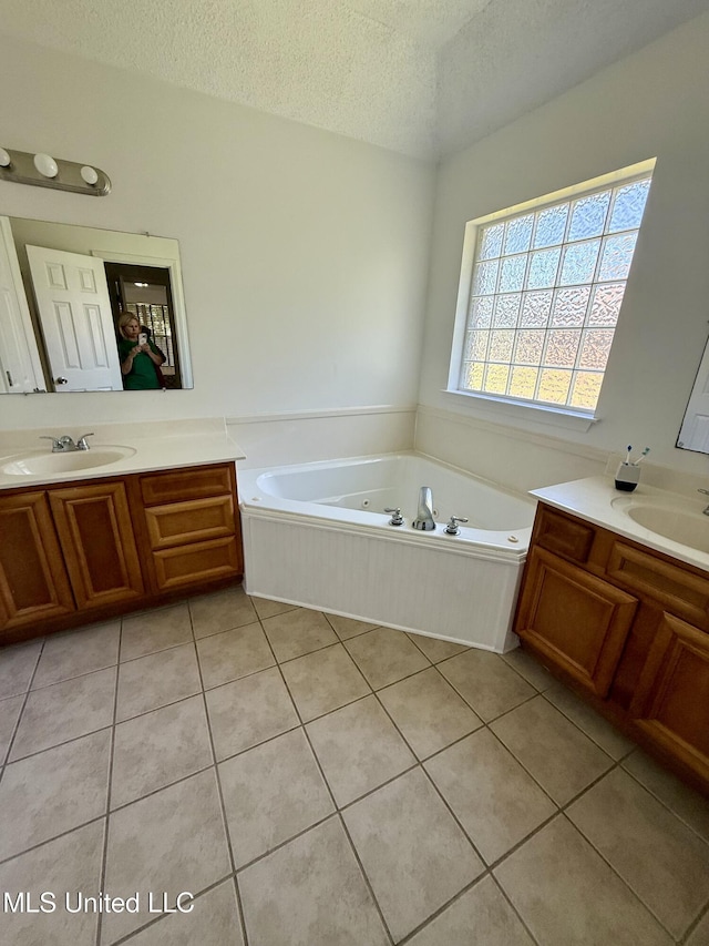 full bathroom featuring a whirlpool tub, a textured ceiling, a sink, and tile patterned floors