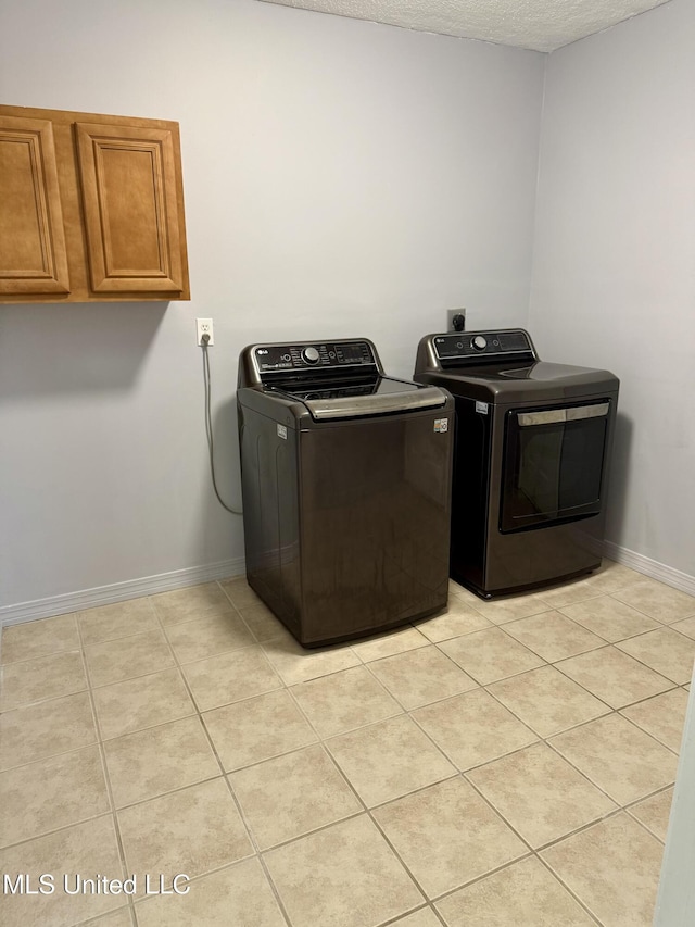 clothes washing area with separate washer and dryer, cabinet space, baseboards, and light tile patterned flooring