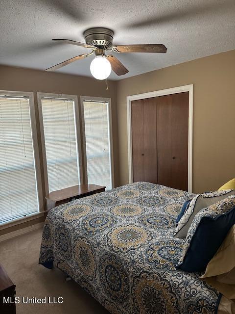 carpeted bedroom with ceiling fan, a closet, and a textured ceiling