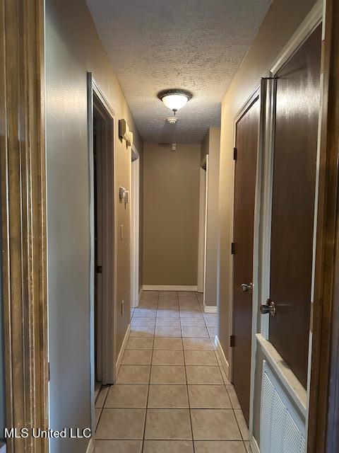 hall with visible vents, baseboards, a textured ceiling, and light tile patterned flooring