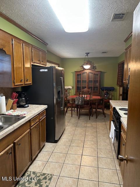 kitchen featuring visible vents, electric range, light tile patterned flooring, tile counters, and stainless steel fridge