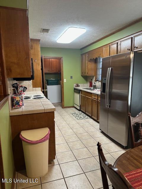 kitchen featuring light tile patterned floors, washer / dryer, stainless steel refrigerator with ice dispenser, white dishwasher, and a sink