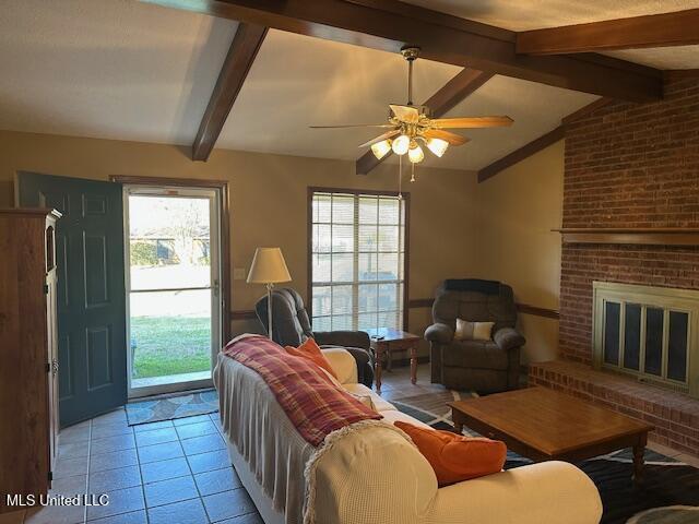 living room featuring vaulted ceiling with beams, a fireplace, light tile patterned floors, and ceiling fan