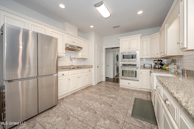 kitchen with visible vents, light stone countertops, under cabinet range hood, decorative backsplash, and stainless steel appliances