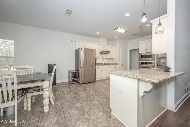 kitchen with visible vents, light stone counters, decorative backsplash, appliances with stainless steel finishes, and a peninsula