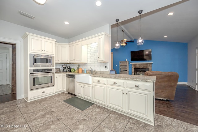 kitchen with a peninsula, a fireplace, a sink, appliances with stainless steel finishes, and open floor plan