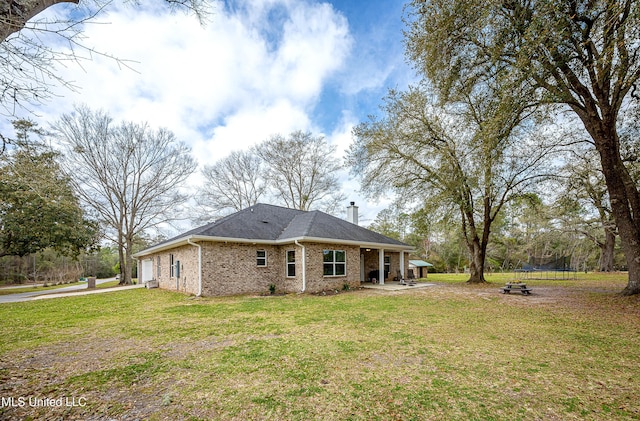 rear view of house with a garage, a yard, brick siding, and a trampoline