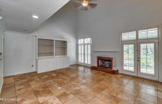 unfurnished living room with french doors, ceiling fan, a towering ceiling, and a brick fireplace